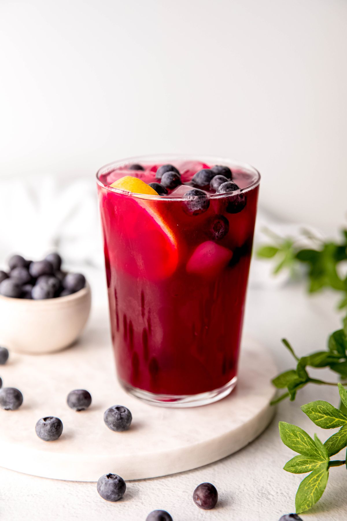 glass of purple-magenta blueberry lemonade garnished with a fresh lemon wheel and whole blueberries.