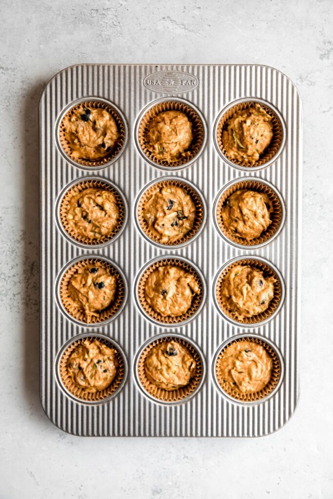 healthy whole wheat blueberry zucchini banana bread muffin batter divvied into 12 wells of a muffin tin.