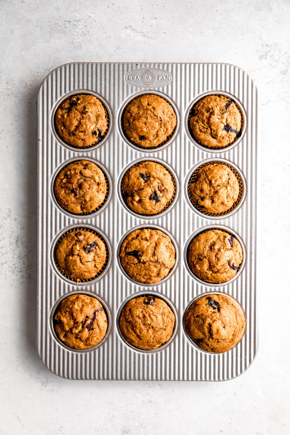 baked blueberry and zucchini muffins in a silver muffin tin after baking.