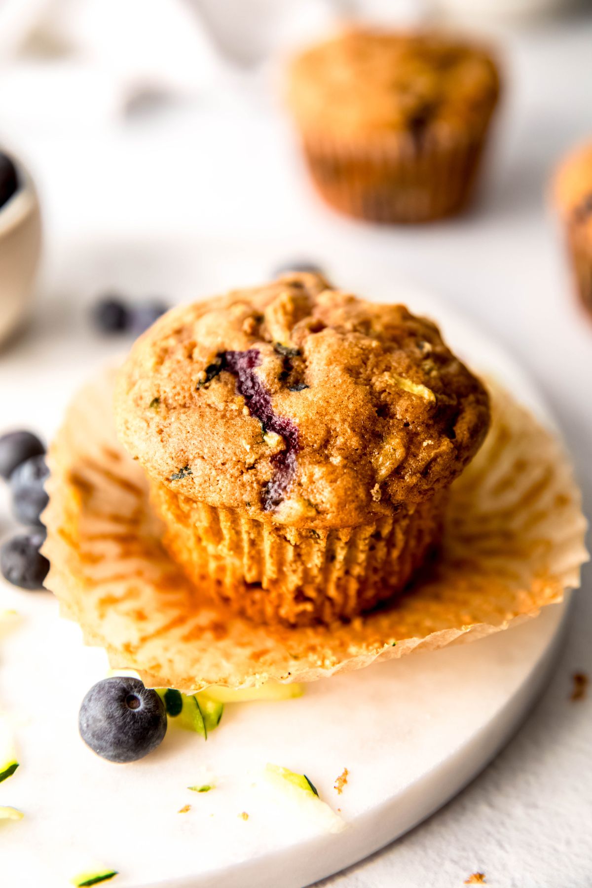 45 degree angle shot of a blueberry zucchini muffin with the kraft paper wrapper pulled away from the sides like a tutu.