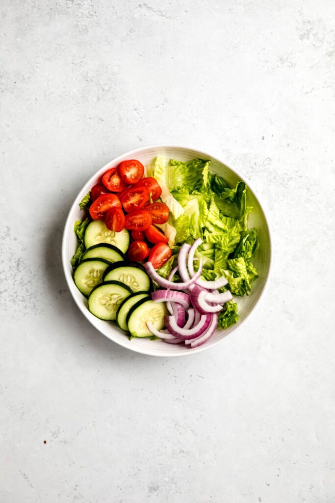 Lettuce, tomatoes, red onions, and cucumbers in a large salad bowl.