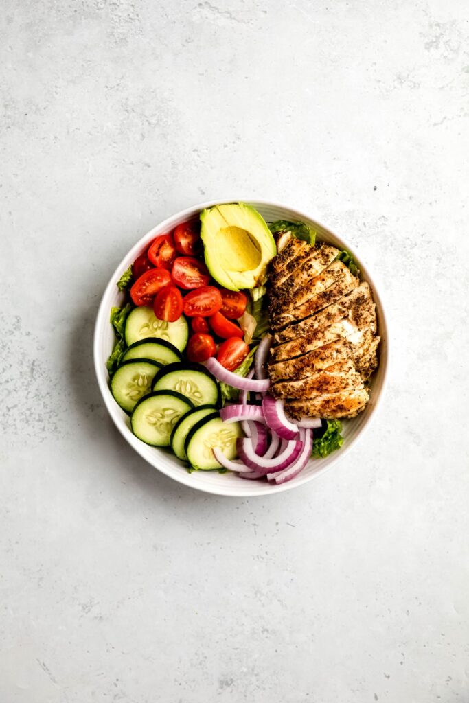 An overhead shot of a bowl of green goddess salad with sliced chicken.