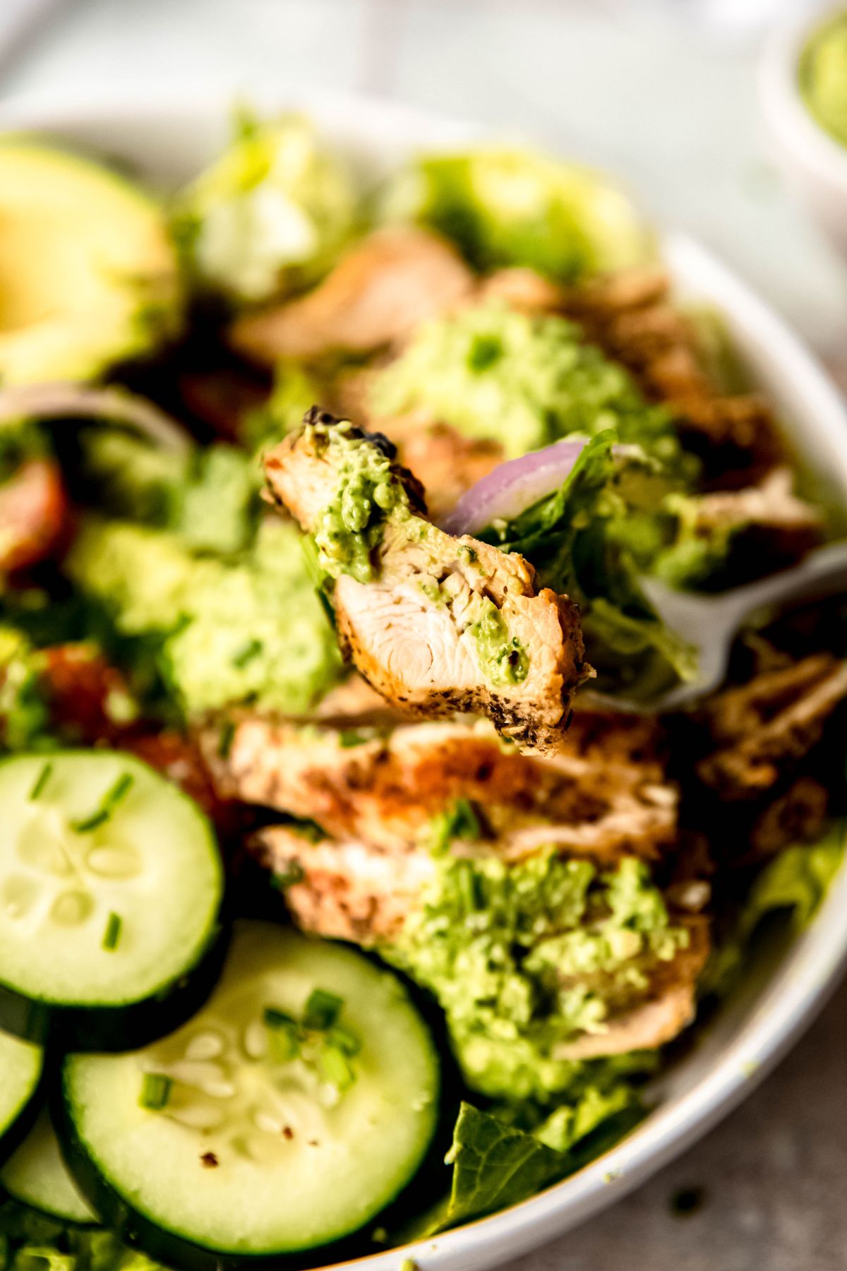 A close-up shot of a bite of grilled chicken with the green goddess salad in the background.