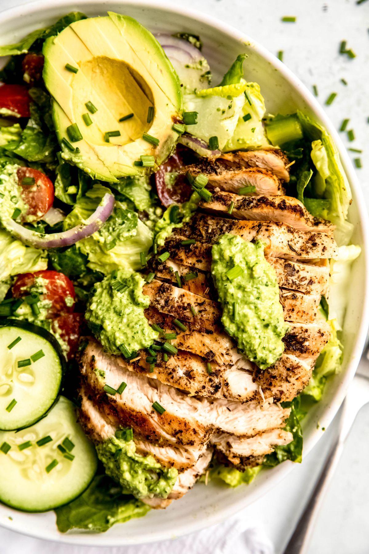 A close-up overhead shot of a bowl of green goddess grilled chicken salad with dressing and chives.