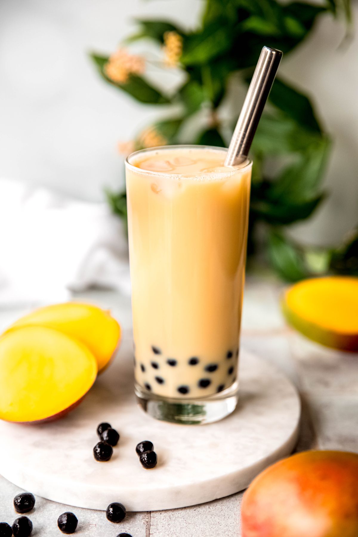 glass of homemade mango milk tea with black boba pearls and a silver bubble tea straw.