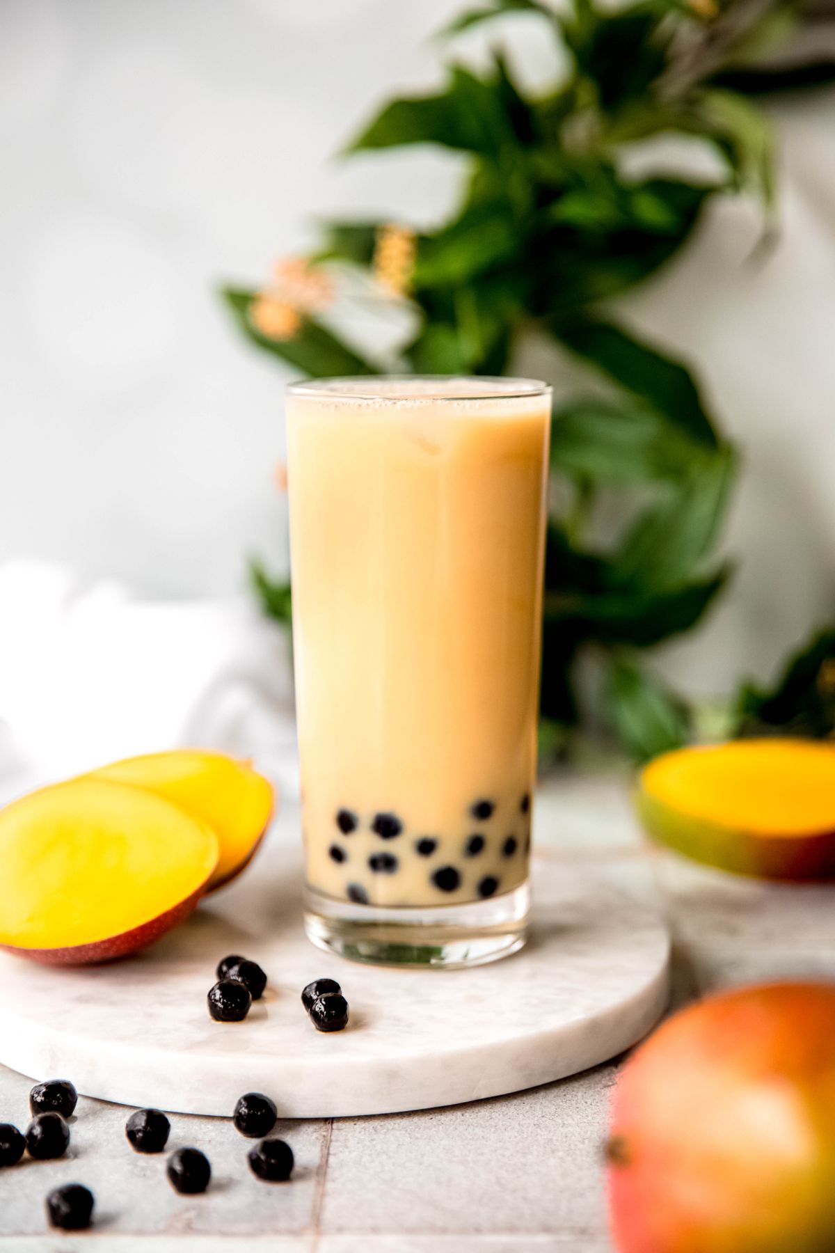 homemade mango milk tea bubble tea on a serving platter with black boba pears and a fresh mango.