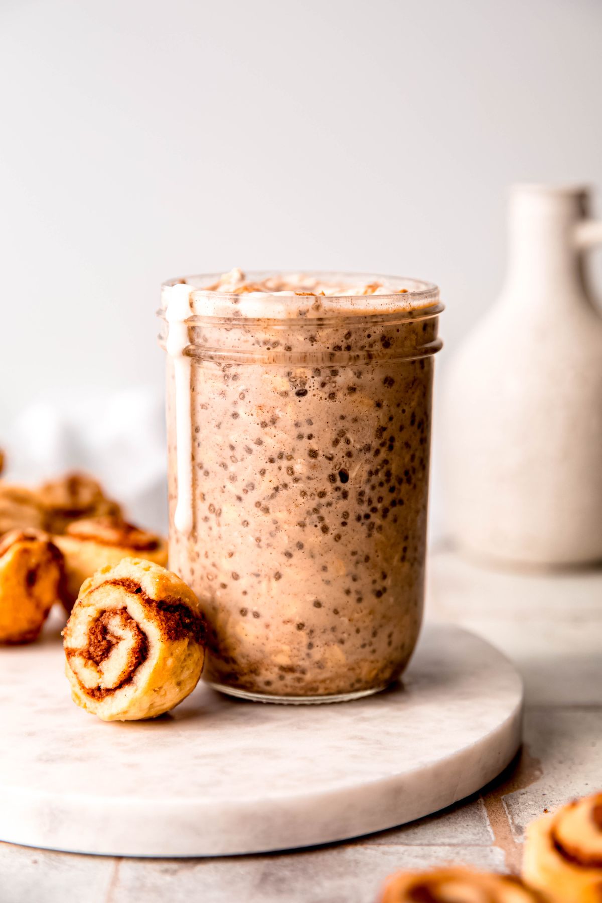 A side shot of a glass of high-protein overnight oats on the counter with a small cinnamon roll bun.