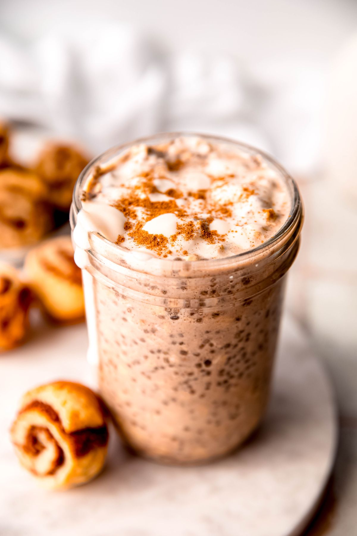 A close-up overhead shot of the high-protein cinnamon roll overnight oats with protein drizzle on the counter with cinnamon roll buns.