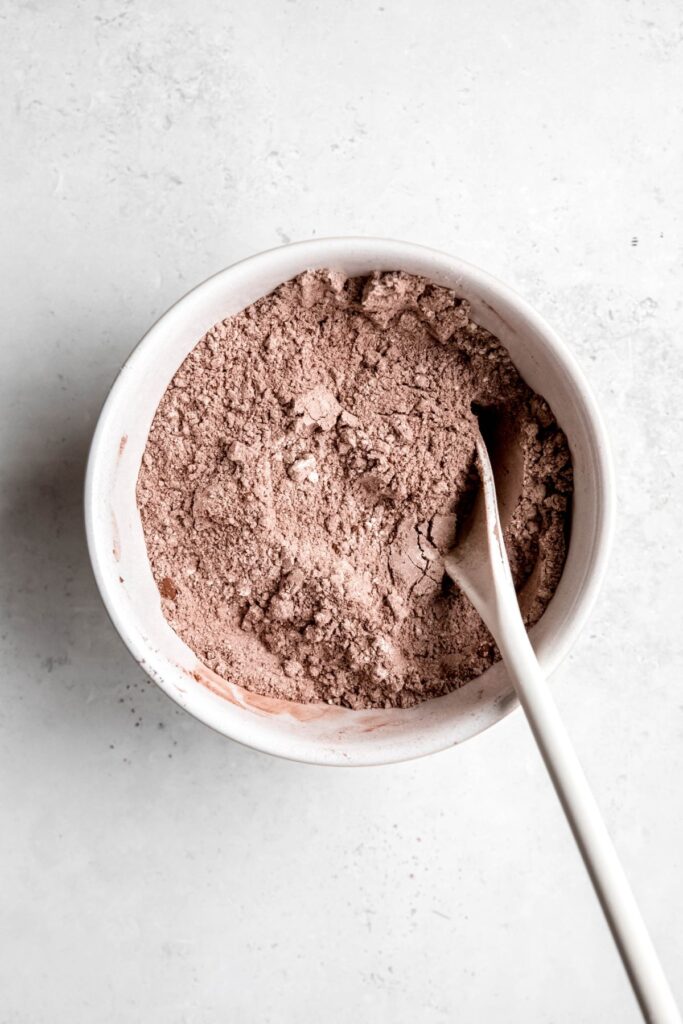 dry muffin ingredients in a white mixing bowl with a wooden spoon.