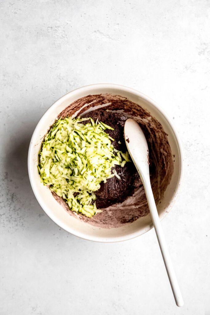 shredded zucchini added to the bowl with dry-looking chocolate muffin batter.
