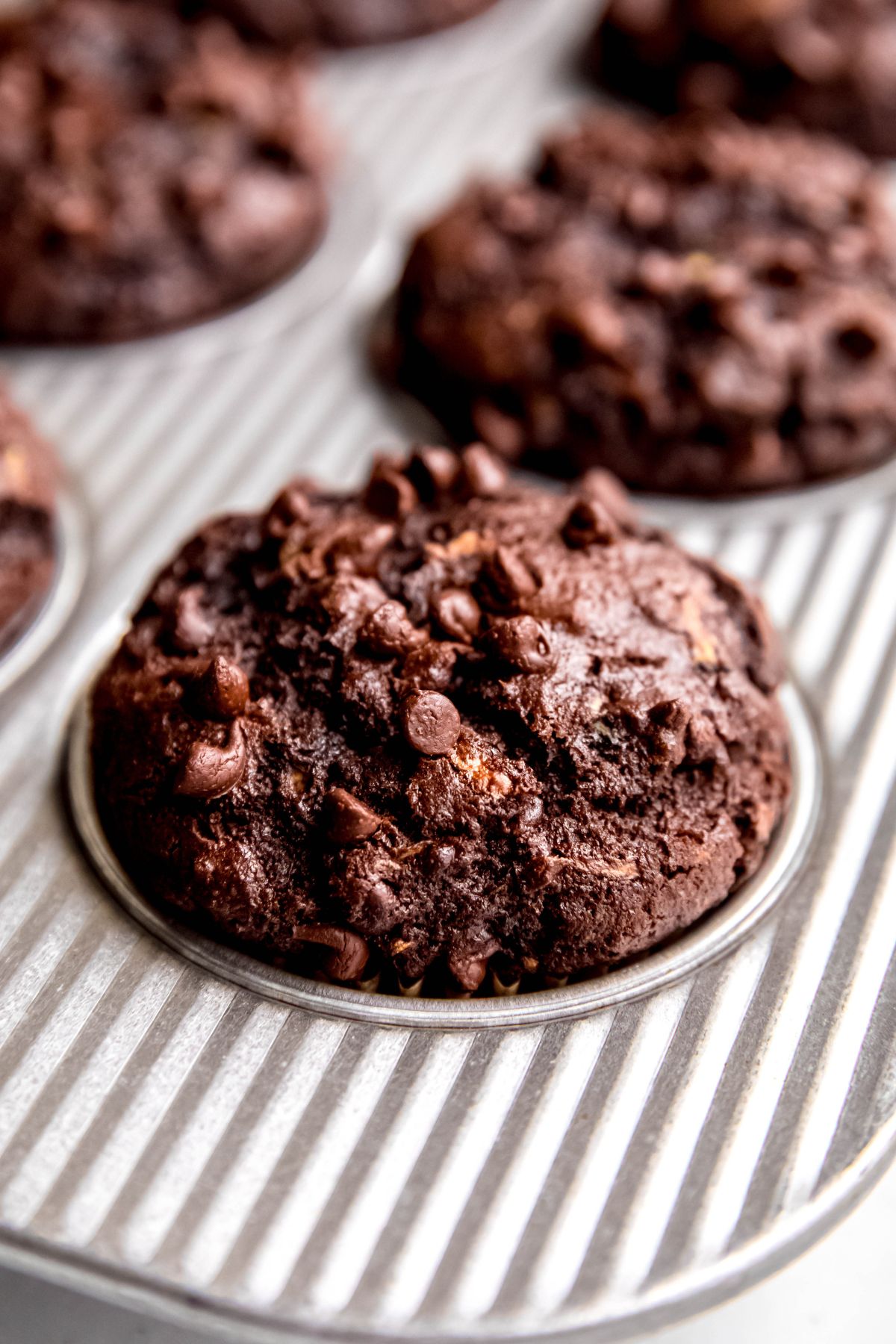 closeup shot on the corner chocolate zucchini chocolate chip muffin in a silver muffin tin after baking.