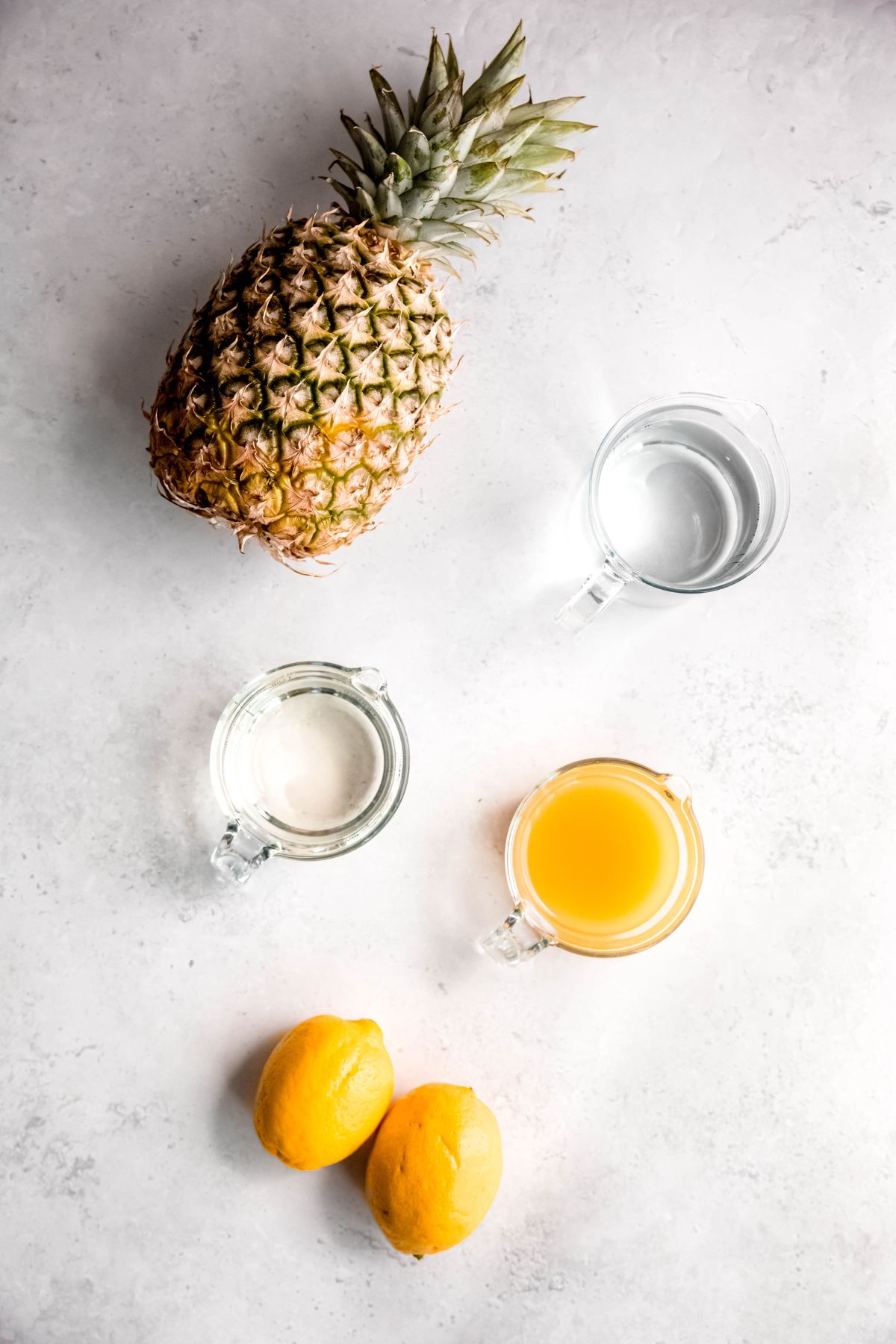 fresh pineapple, fresh lemons, simple syrup, pineapple juice, and water measured out for making pineapple lemonade recipe.