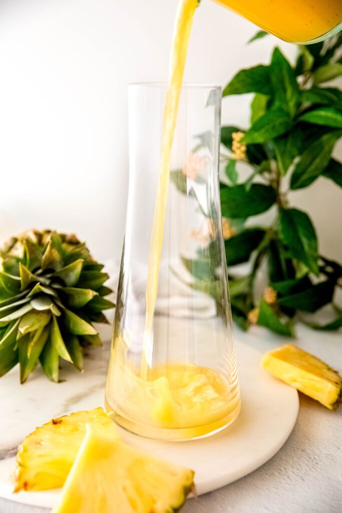 action shot of pineapple mixture and lemon juice being added to a pitcher.
