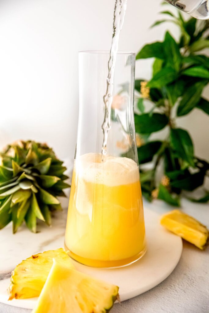 action shot of water and simple syrup being added to the pitcher with the pineapple lemon juice.
