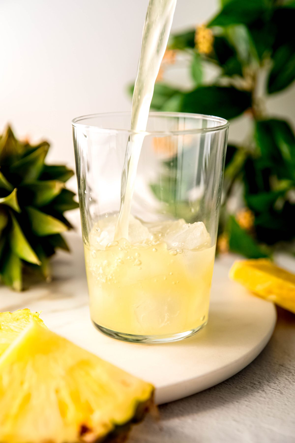 action shot of pineapple lemonade being poured over a glass of ice for serving.