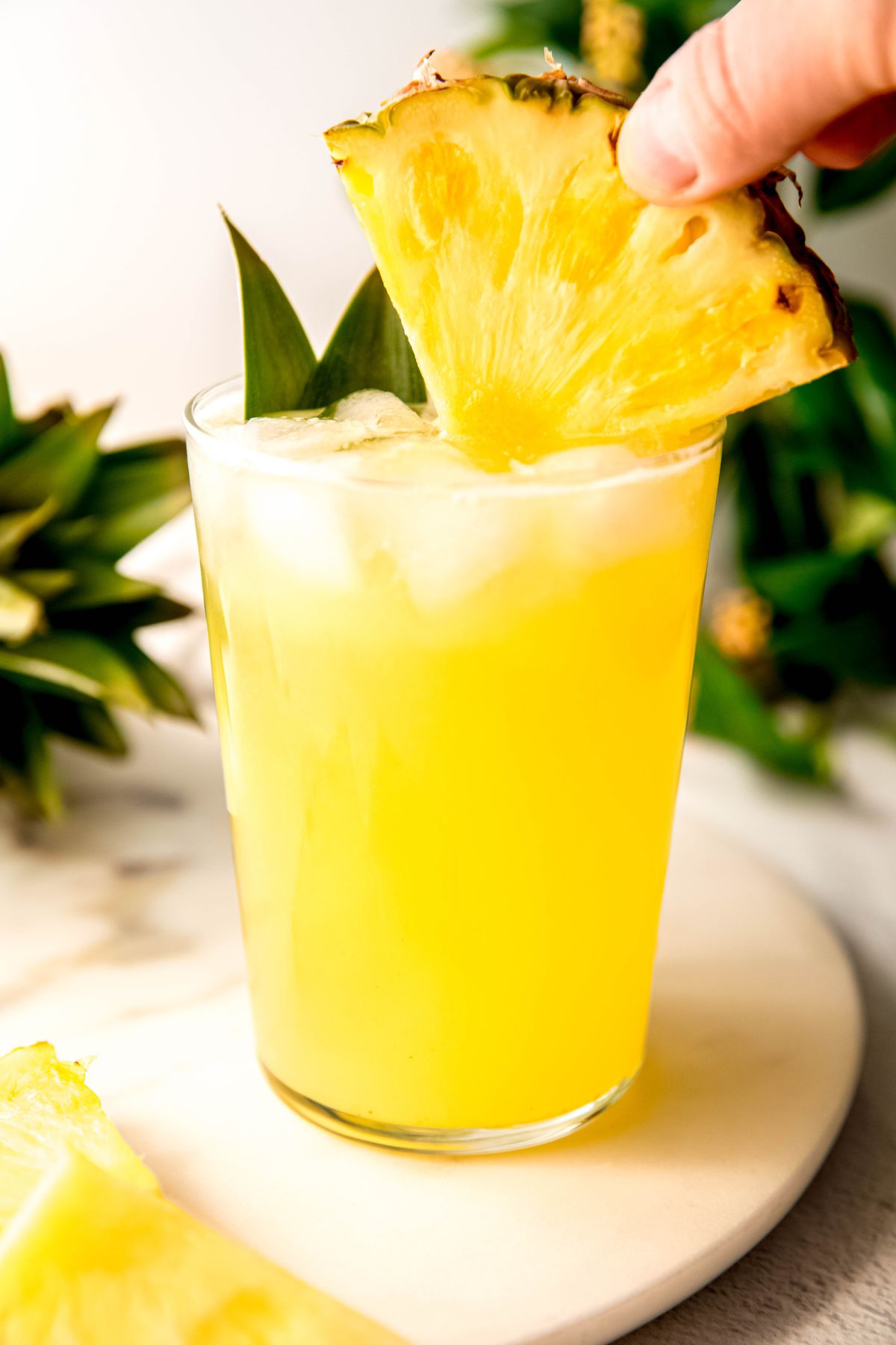 hand dunking a fresh wedge of pineapple in the glass of pineapple lemonade.