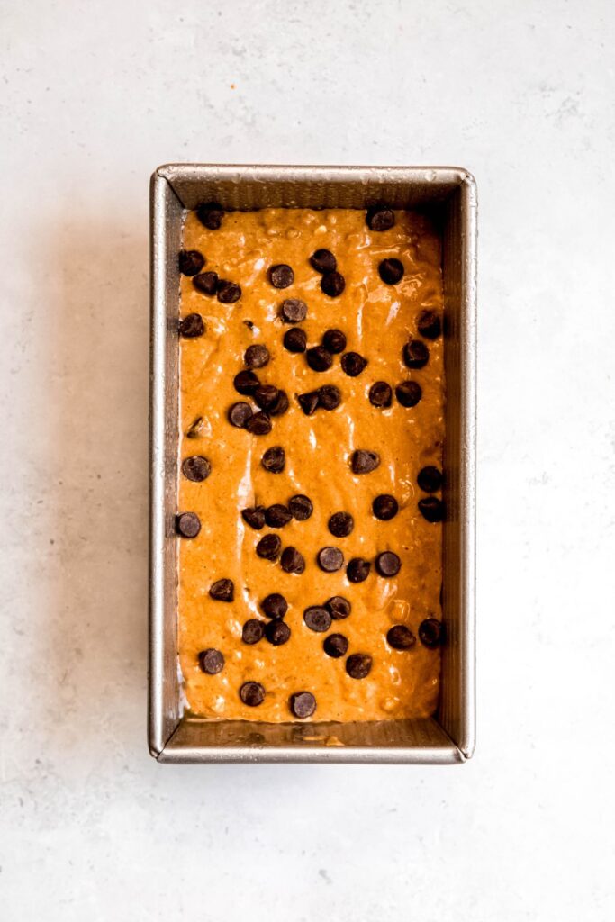 high protein banana bread batter added to a metal loaf tin and topped with extra chocolate chips.