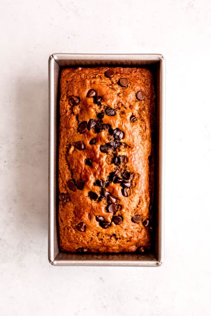 baked banana bread with protein powder and chocolate chips in a loaf tin on a white table.