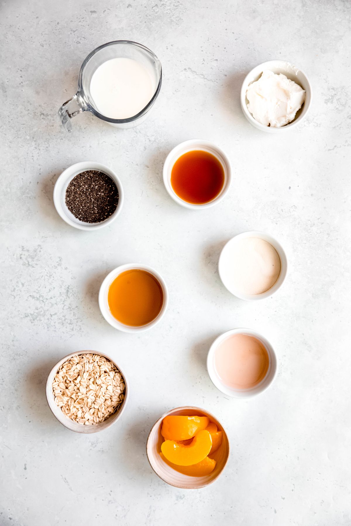 ingredients for making peach overnight protein oats measured out into bowls on a white table.