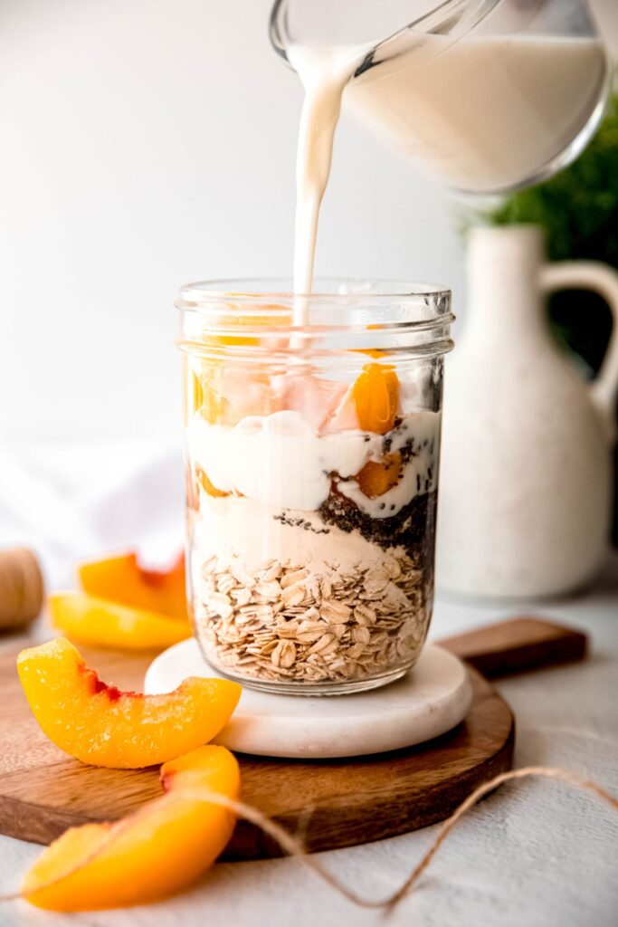 action shot of milk being poured into the jar with the other peach overnight oats ingredients.