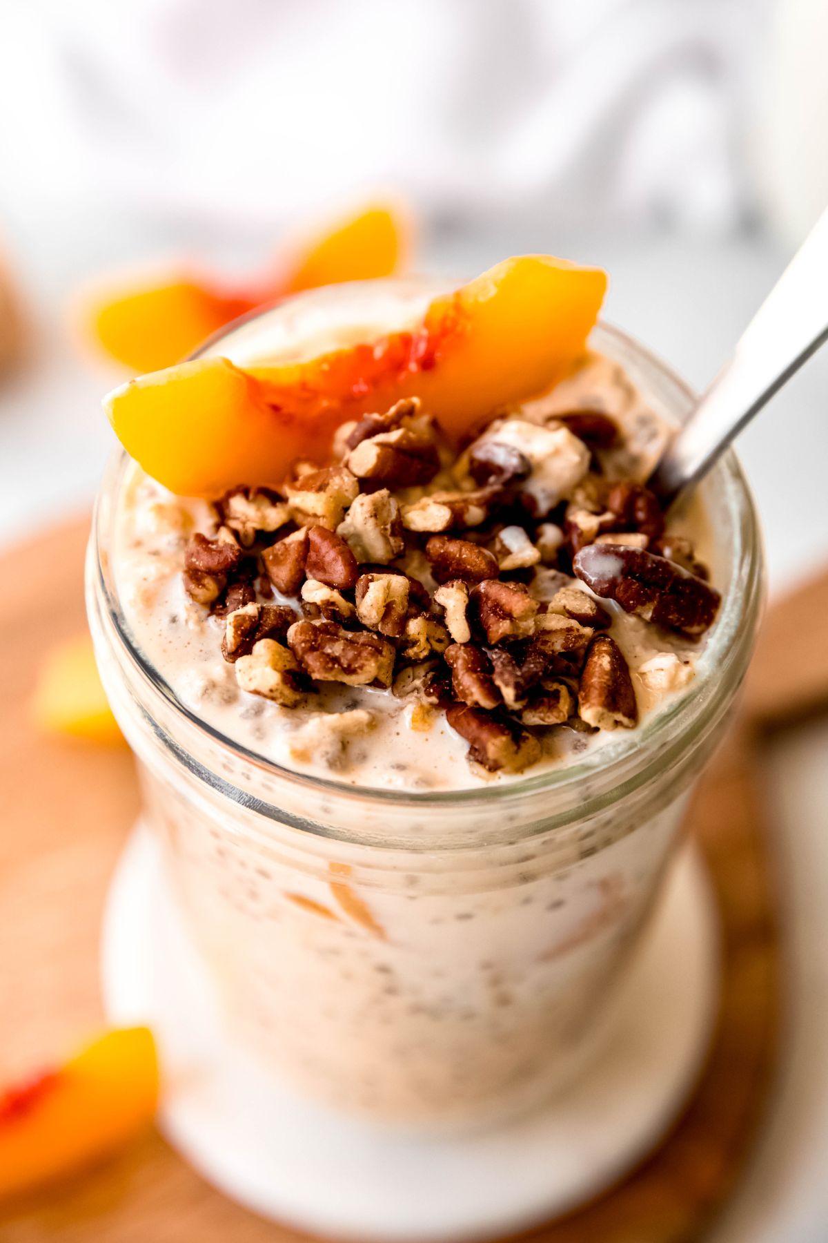 45 degree downward closeup shot of the pecans and peach slices atop the jar of peaches and cream protein oats with a silver spoon sticking out.
