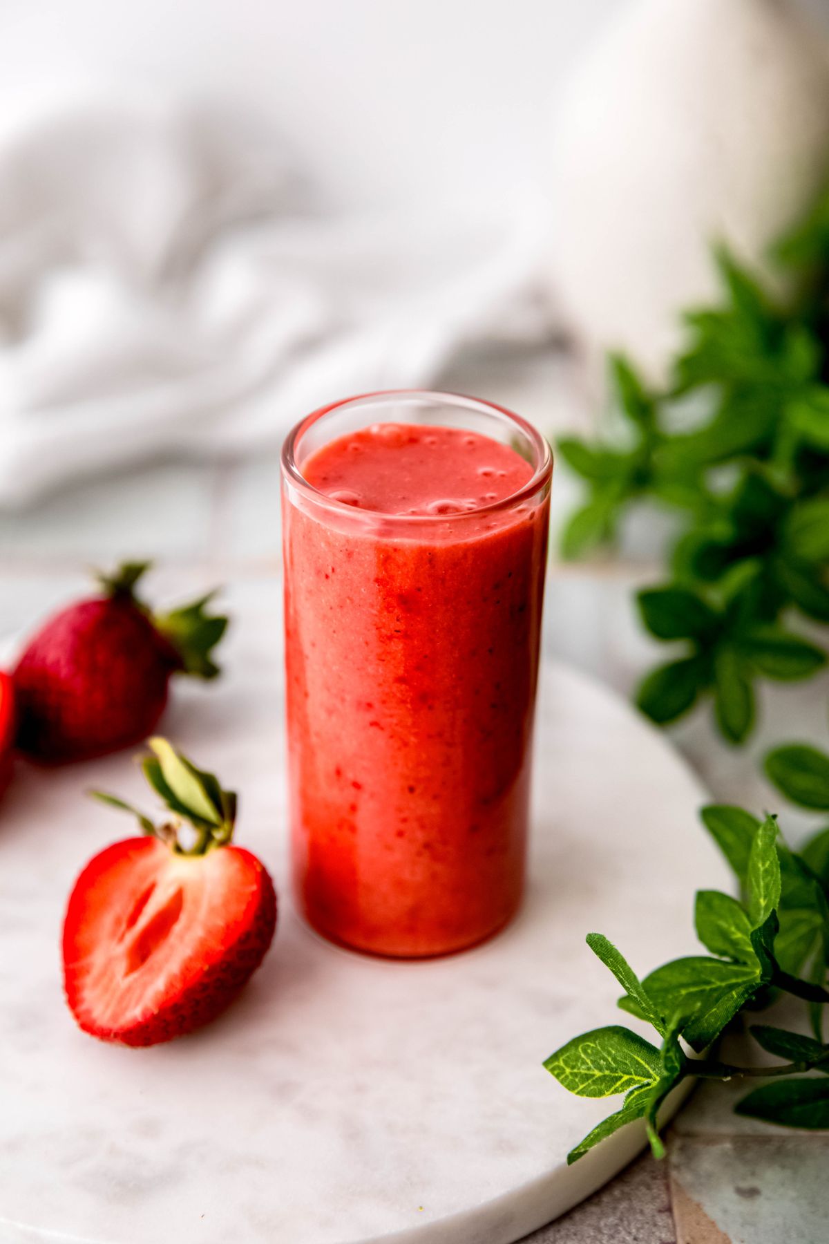 An angled shot of a glass of strawberry vinaigrette on the counter with greens and halved berries.