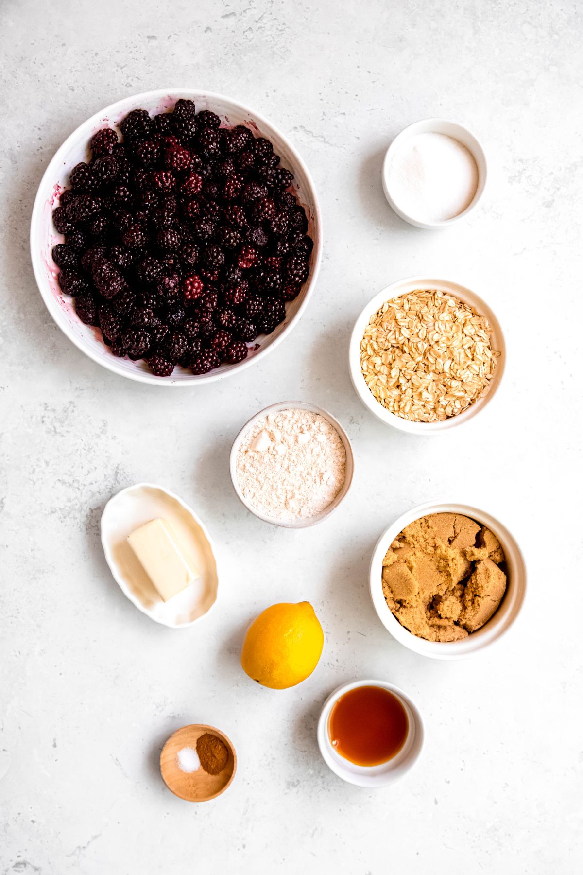 ingredients needed to make fresh blackberry crisp recipe measured out into bowls on a white table.