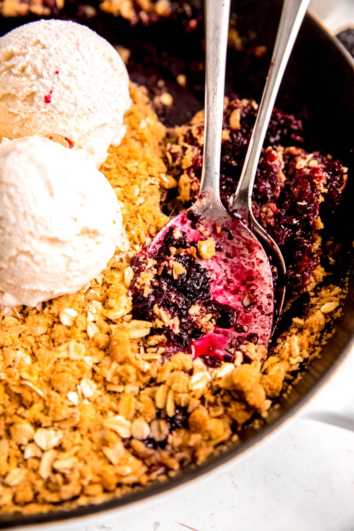 closeup shot of 2 silver serving spoons in the skillet blackberry crisp showing the jammy texture of the filling.