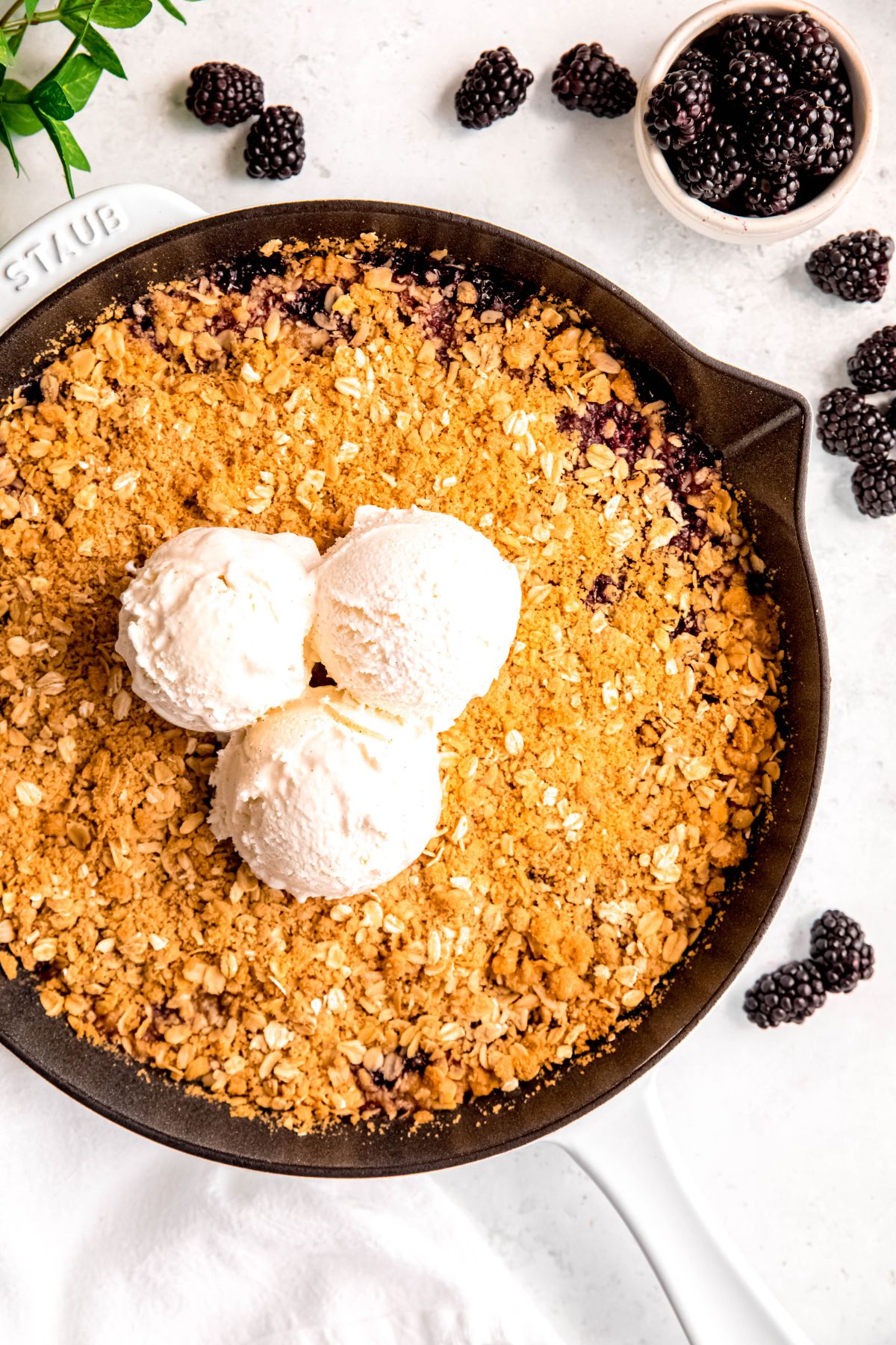 closeup shot of a cast iron blackberry crisp topped with vanilla ice cream.