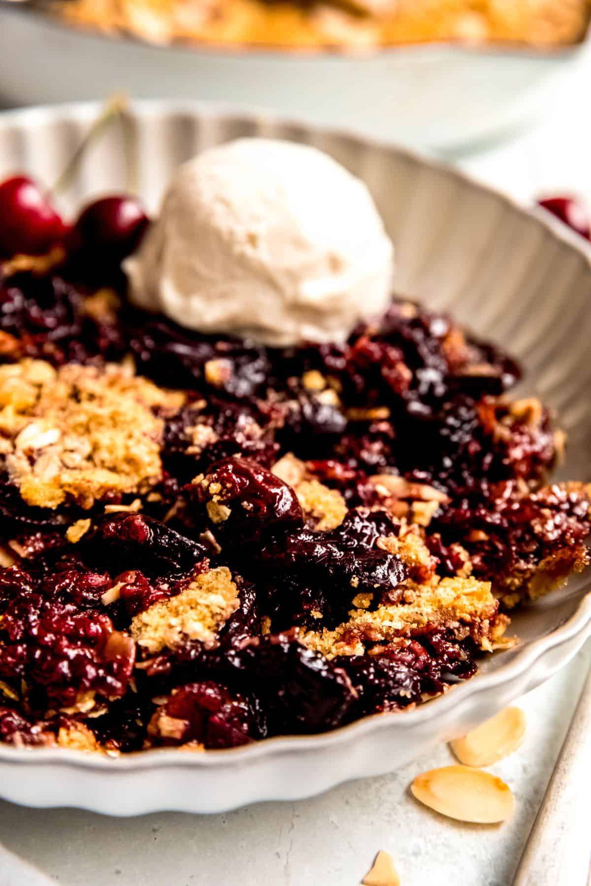 A close-up shot of a serving bowl of fresh cherry crisp with a scoop of ice cream.