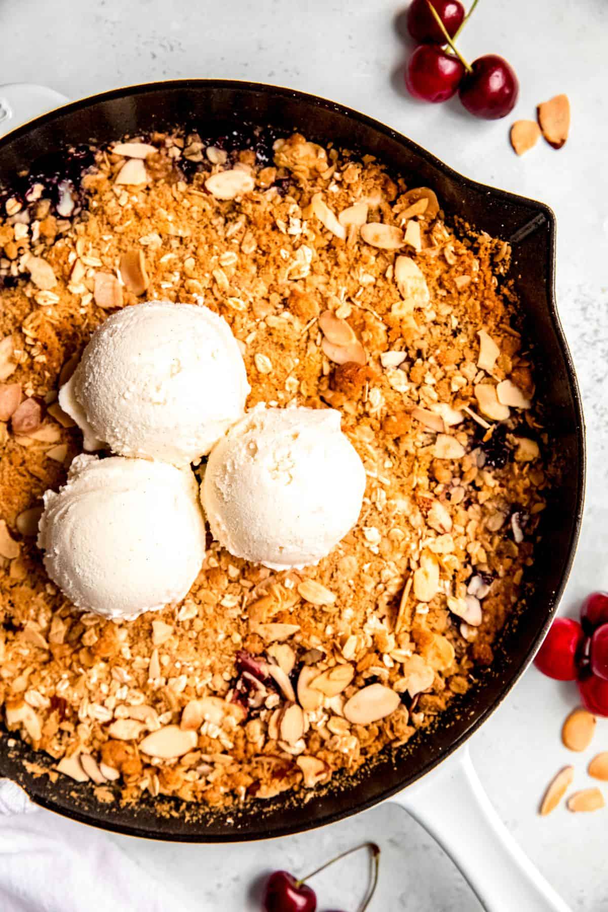 A close-up overhead shot of a pan of cherry crisp with 3 scoops of ice cream.
