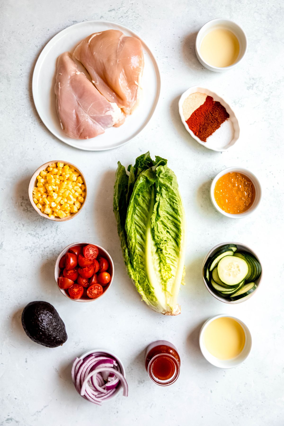 ingredients needed for making grilled hot honey chicken salad measured out into white bowls and plate on a grey-white table.