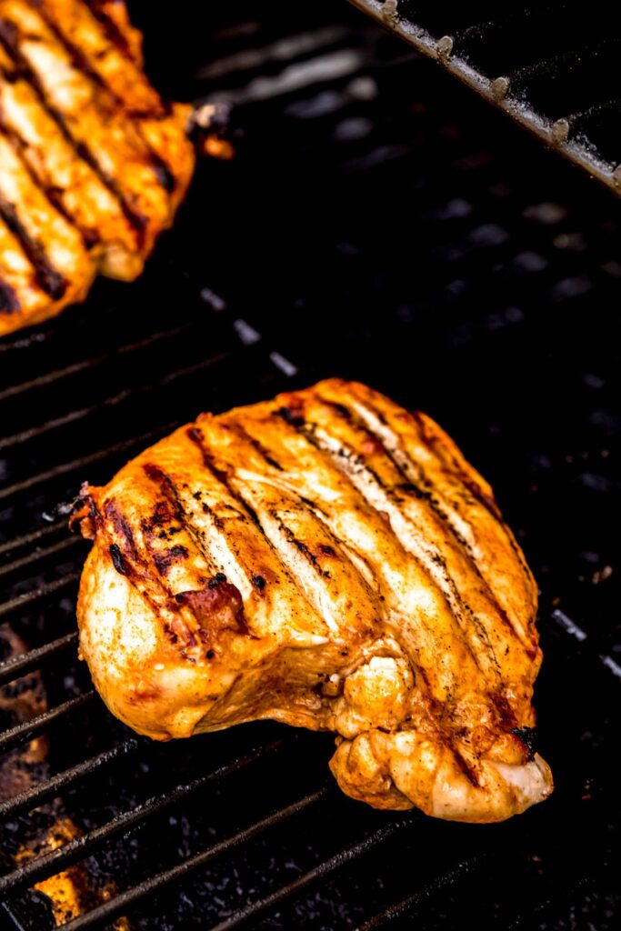 hot honey chicken breasts on the grill; they have been flipped once, revealing char marks.
