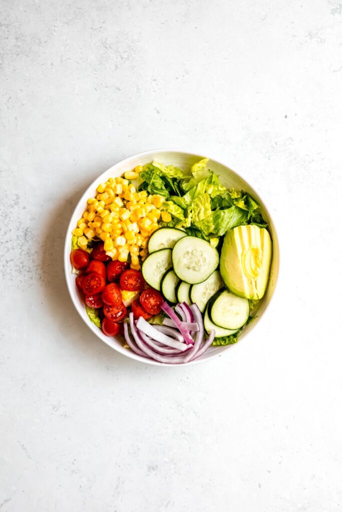 corn, cherry tomatoes, sliced red onions, cucumbers, and avocado grouped on top of the bed of romaine.