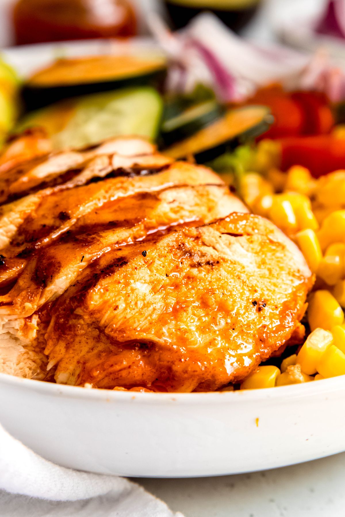 closeup shot of the hot honey chicken slices in the salad bowl; they're glazed and juicy-looking and are surrounded by corn kernels on the right.