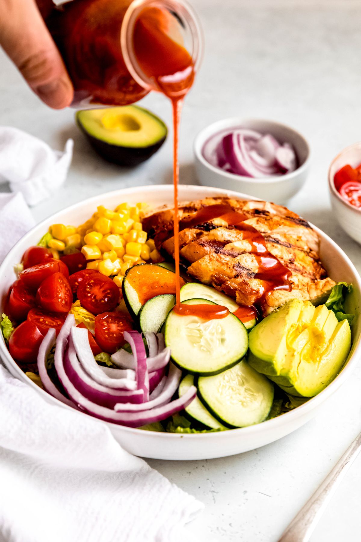 action shot of a hand pouring the hot honey vinaigrette over the composed hot honey salad; there's a line of it across the chicken breast slices and it's being drizzled on the cucumber slices.