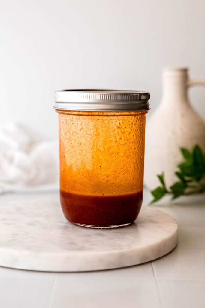 mason jar with a silver lid secured and hot honey dressing running down the sides after shaking to combine.
