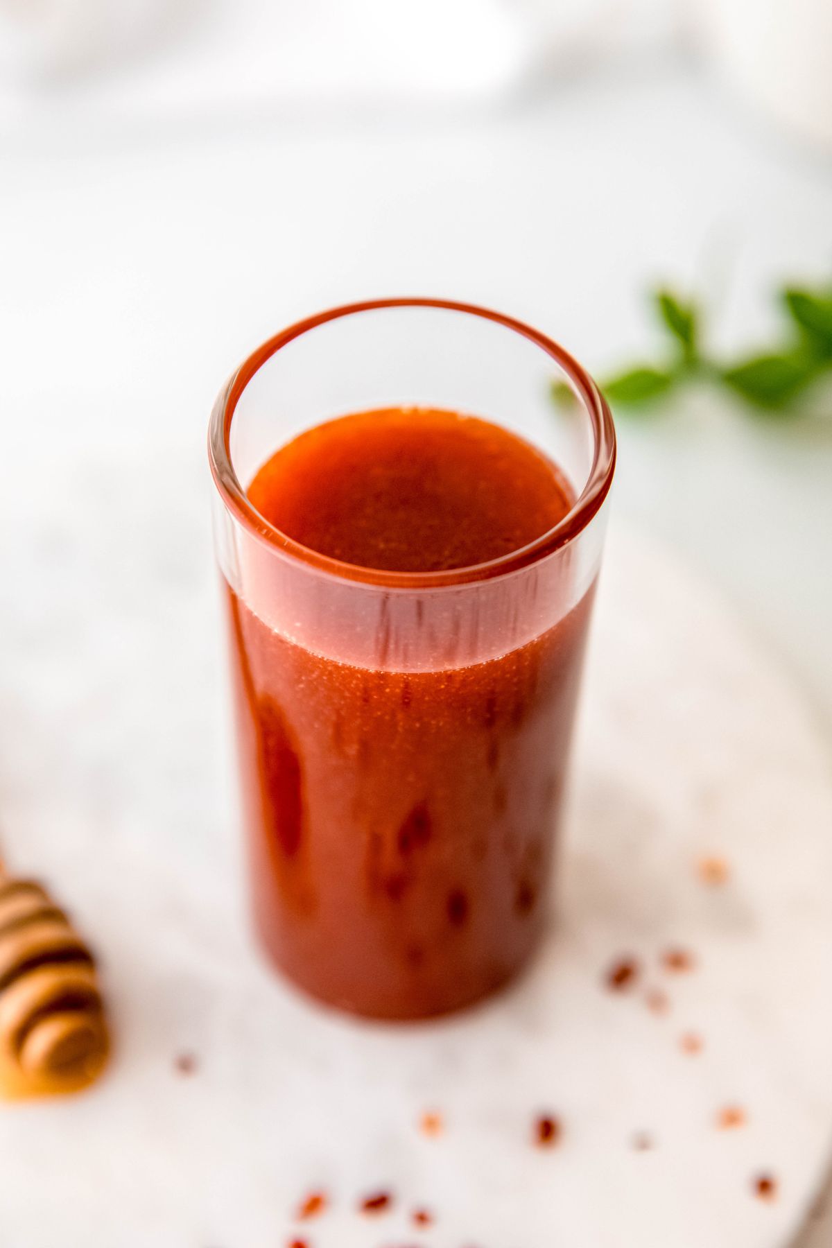 45 degree downward shot into a glass of hot honey dressing; it looks brownish red and has a thick, viscous consistency.