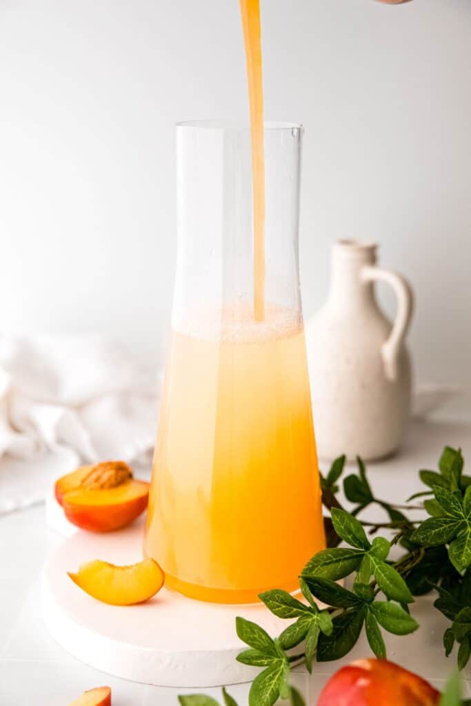 action shot of nectarine syrup being poured into the lemon water.