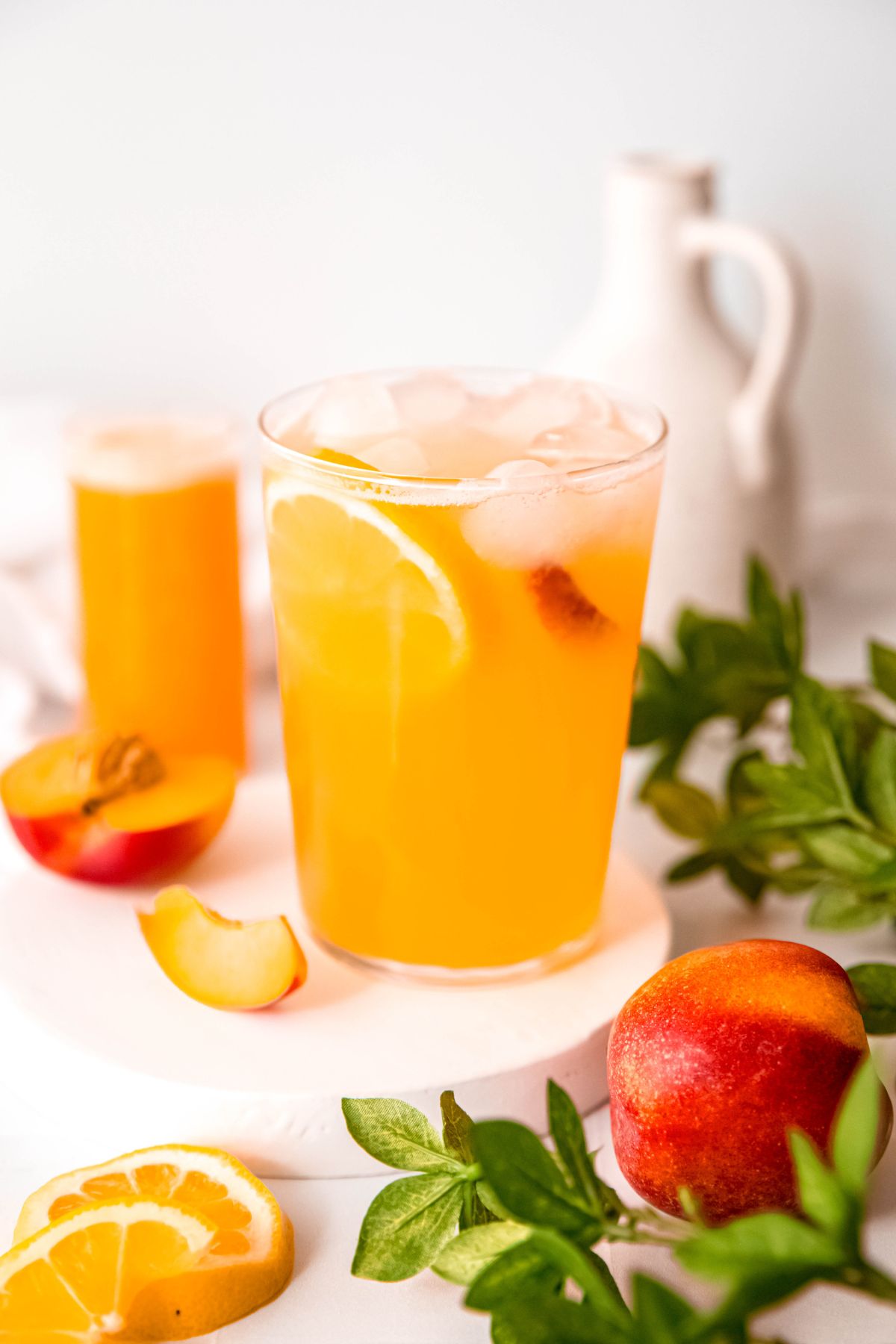 hero shot of nectarine lemonade in a pint glass with ice, lemon wheel and fresh nectarine.