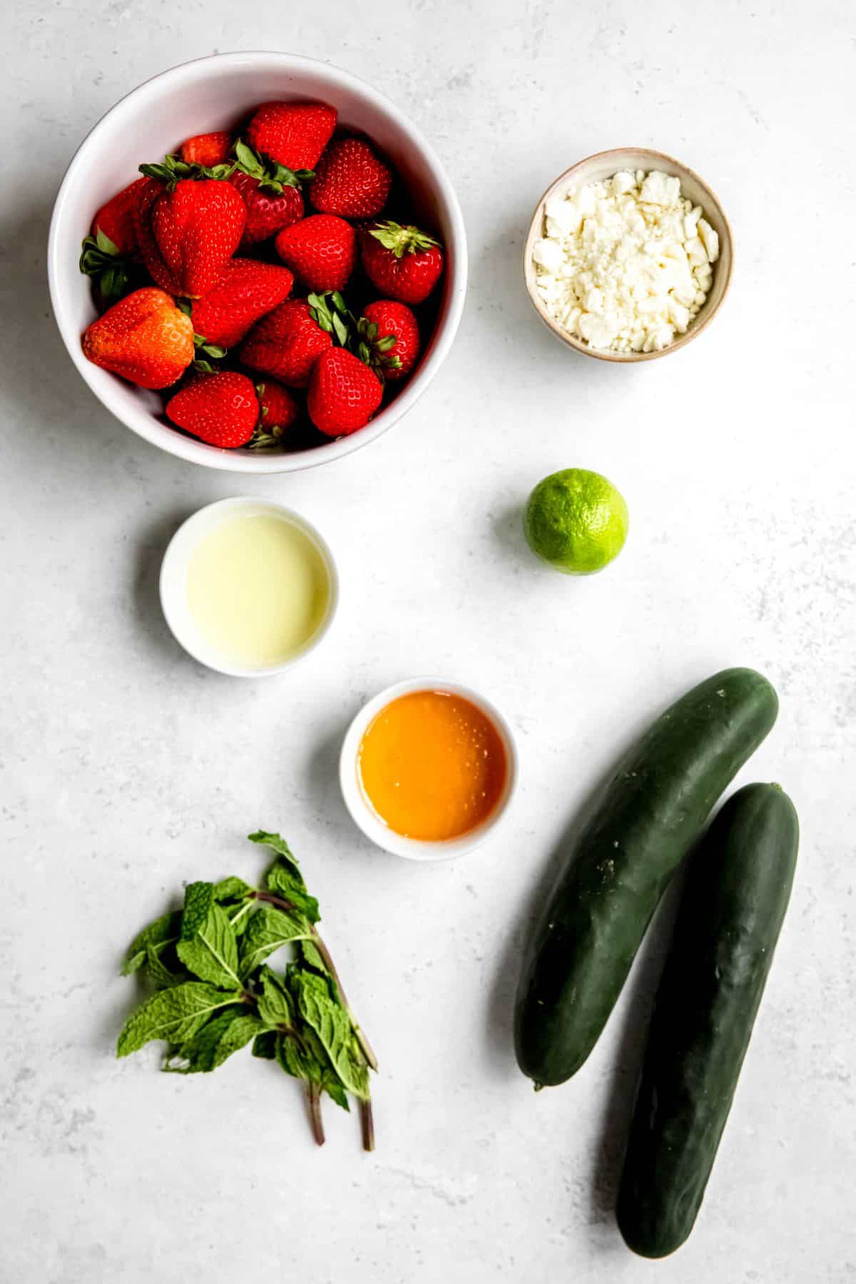 strawberries, cucumbers, feta, mint, fresh lime, oil, and honey measured out for making strawberry and cucumber salad.
