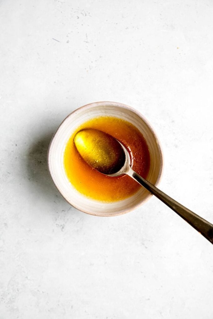 salad dressing ingredients combined in a small mixing bowl with a silver spoon.