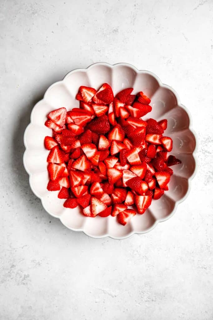 halved strawberries added to a large white scalloped serving dish.
