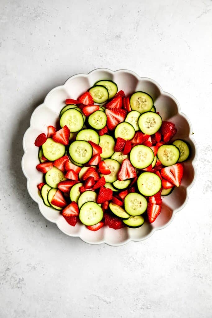 sliced cucumbers added to the salad bowl with the strawberries.