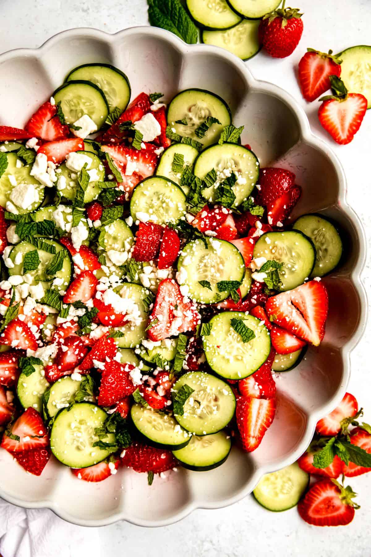 closeup overhead shot of the right 4/5 of a serving bowl of cucumber strawberry salad garnished with cheese and shredded mint.