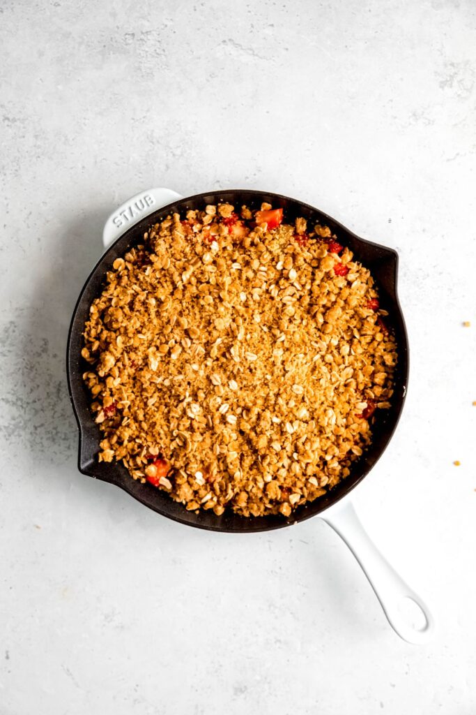 A large white skillet of strawberry rhubarb crisp before baking.