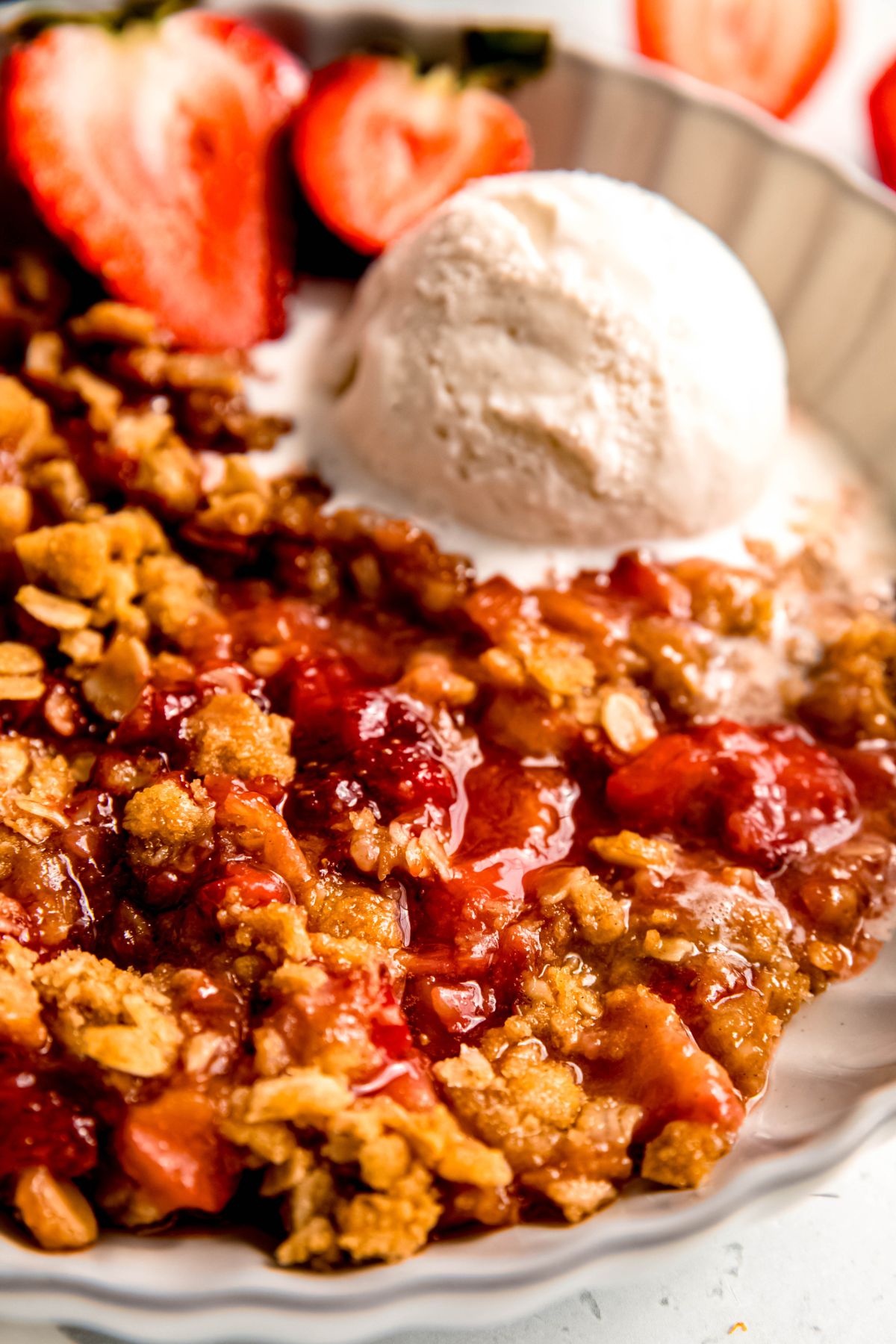 A close-up shot of a serving of strawberry rhubarb crisp with a scoop of vanilla ice cream.