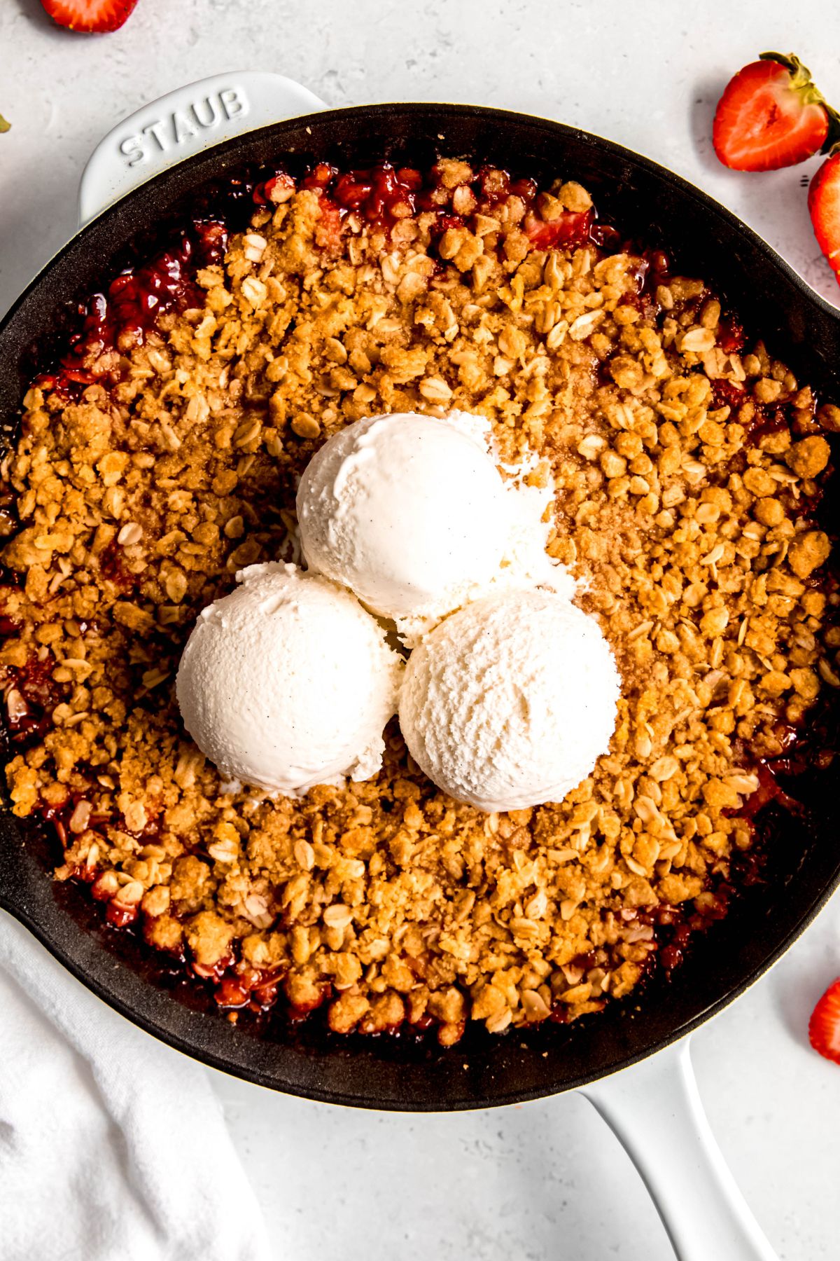 An overhead shot of a pan of strawberry rhubarb crisp with 3 scoops of vanilla ice cream.