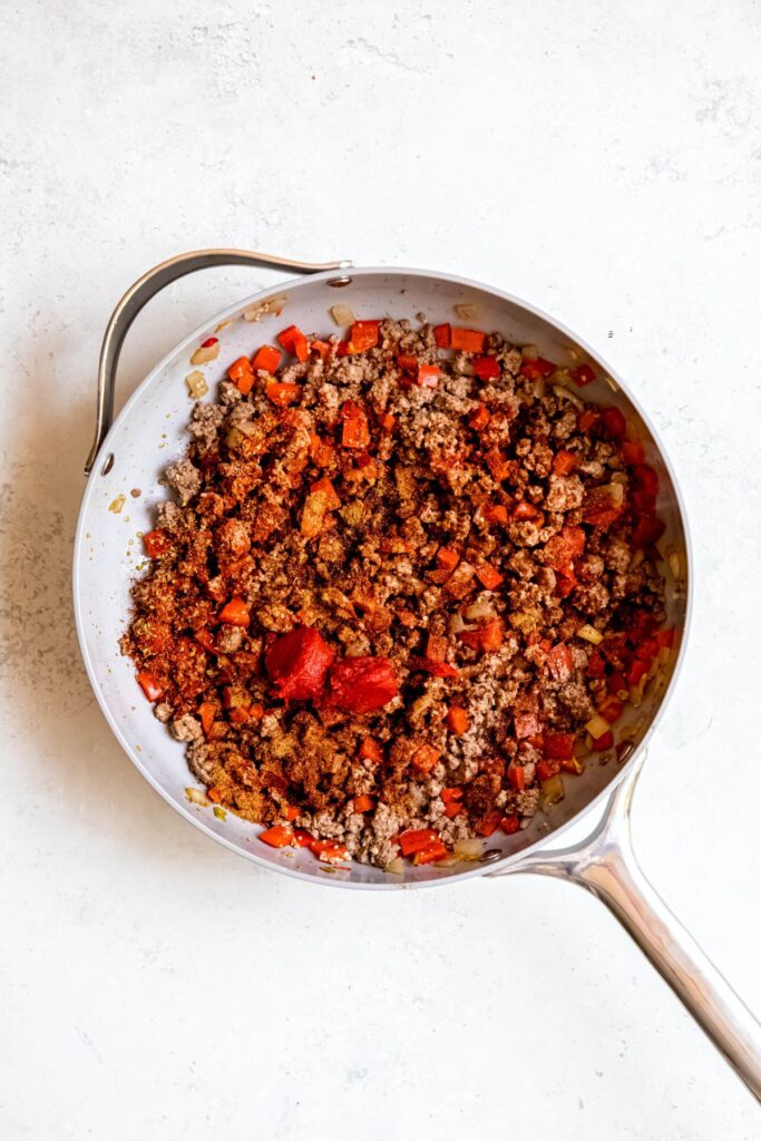 Adding the tomato paste to the crumbled meat and veggies.