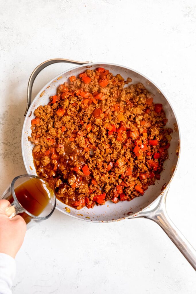 Pouring the beef broth into the pan of ground beef and veggies.